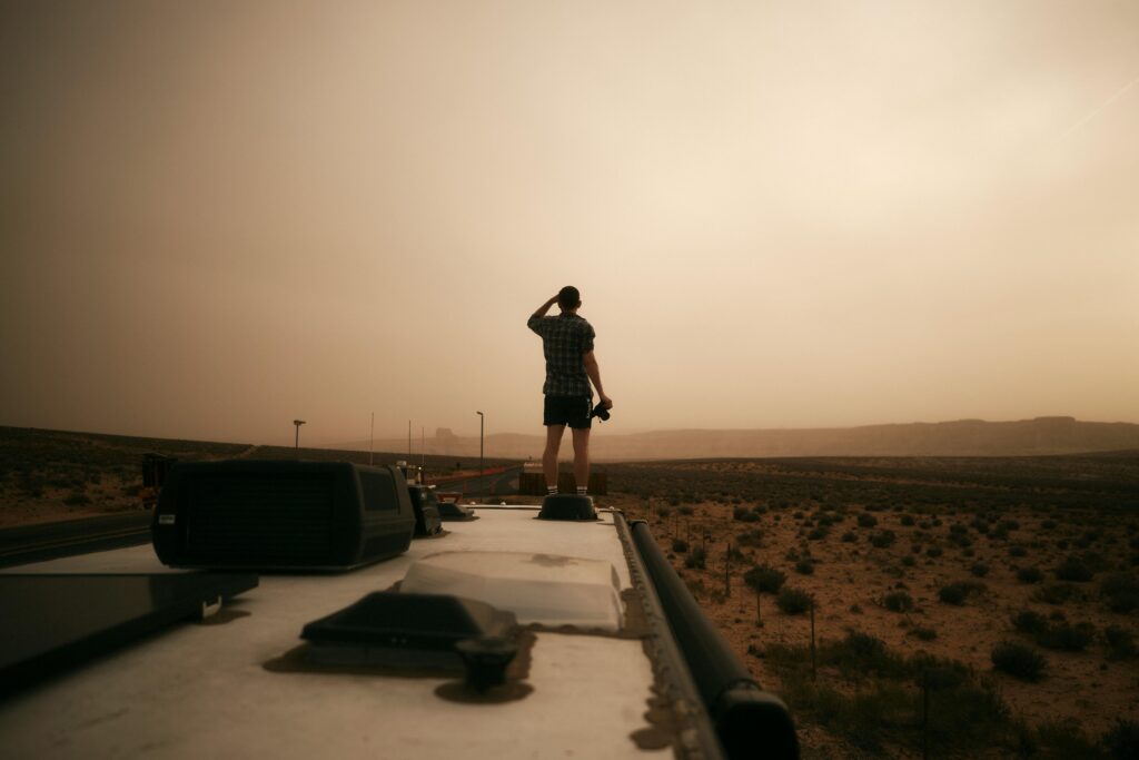 Traveler standing on an RV roof, gazing at the Arizona desert during evening light, evokes a sense of adventure.