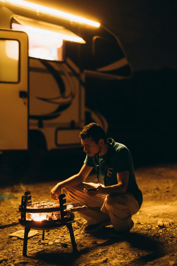 A man cooking barbecue by an RV at night in the desert of Showkah, UAE.