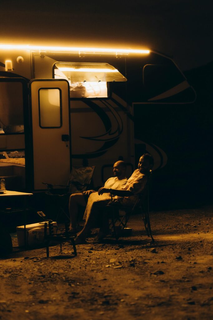 Two individuals enjoy a peaceful evening outside their RV, enveloped by warm light in Showkah, UAE.
