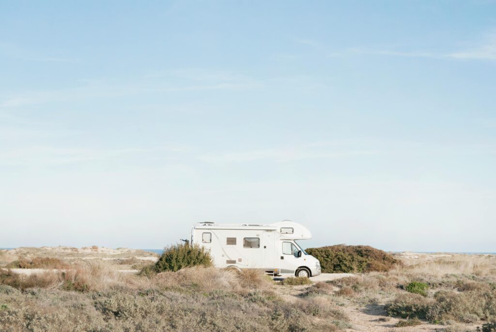 A serene view of an RV parked in a dry landscape, under a clear blue sky.